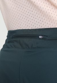 Tmavě modré sportovní šortky s hladkým elastickým páskem a malou zipovou kapsou. Materiál je lehký a prodyšný.