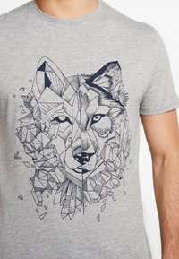 Camiseta gris con un diseño geométrico de lobo en azul oscuro, con formas angulares y texturas facetadas que rodean la cara del lobo.