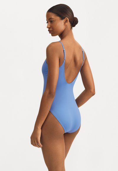 Maillot de bain une pièce bleu avec de fines bretelles, design à dos nu, texture lisse et coutures minimales, mettant en valeur une silhouette élégante.
