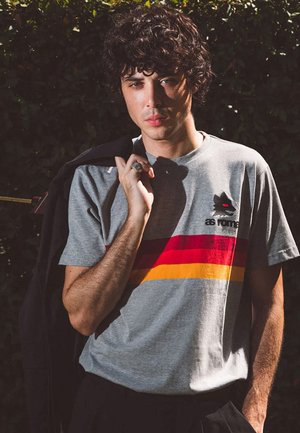 Grijze katoenen t-shirt met rood en gele horizontale strepen en een kleine zwarte afbeelding van een wolf gezicht. Gestyled met een donkere jas.