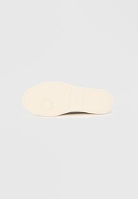 Shoe sole in light beige rubber with a smooth texture, featuring an embossed circular detail and a subtle tread pattern for grip.