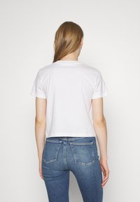 Bílý zkrácený tričko s krátkým rukávem a kulatým výstřihem, spojené s modrými skinny džíny. Hladká textura, minimalistický design.