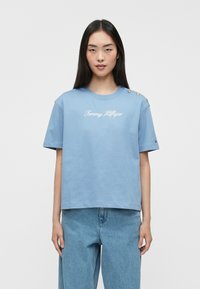 Gaišzils kokvilnas T-krekls ar īsām piedurknēm, ar apaļu kakla izgriezumu, izšūtu "Tommy Hilfiger" logotipu un zelta pogu akcentiem uz pleca.