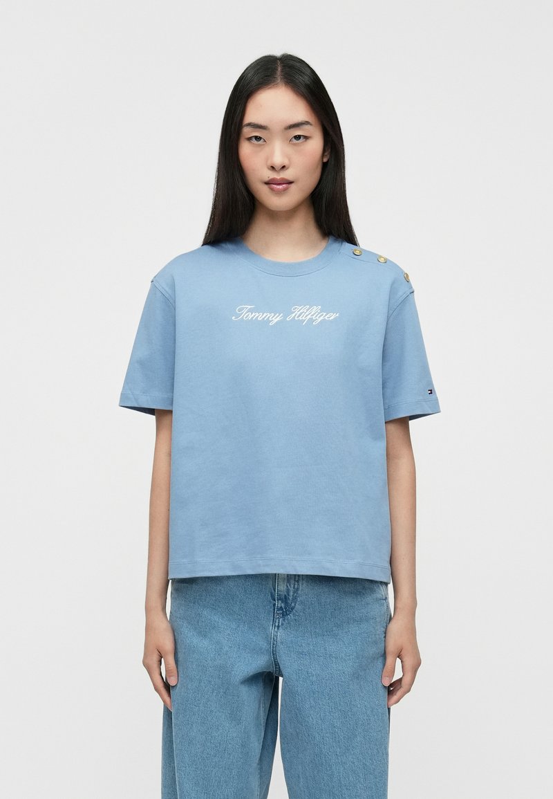 Gaišzils kokvilnas T-krekls ar īsām piedurknēm, ar apaļu kakla izgriezumu, izšūtu "Tommy Hilfiger" logotipu un zelta pogu akcentiem uz pleca.