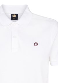 Polo bianco realizzato in cotone, con colletto bottonato e una toppa con logo con accenti rossi e blu sul petto.
