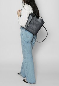 Sac à dos texturé bleu marine avec une surface perforée, un cordon de serrage en haut et une poche zippée. Assorti à un jean en denim clair taille haute.
