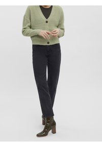 Zielony sweter na drutach z dekoltem w serek i zapięciem na drewniane guziki, zestawiony z czarnymi dżinsami o prostych nogawkach i wysokim stanie oraz błyszczącymi zielonymi botkami do kostki.