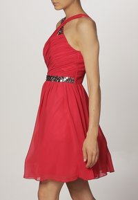 Red sleeveless dress with a fitted, pleated bodice, a jeweled waistline, and a flowing skirt. Smooth fabric with a subtle sheen.