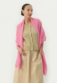 Châle rose drapé sur un haut en tricot beige à col rond et à fermeture à boutons, associé à une jupe beige. Texture lisse et design simple.