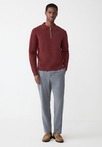 Pull en maille bordeaux avec col et demi-fermeture éclair ; pantalon gris ajusté ; mocassins marron clair ; texture lisse et coupe ajustée.