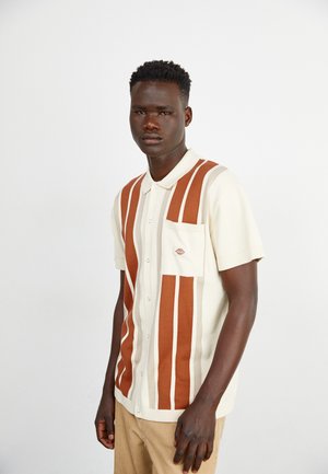 Polo de manga corta con diseño de rayas verticales en blanco, marrón y beige, que cuenta con un bolsillo frontal, botones y un detalle de logo.