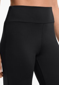 Hochgeschnittene schwarze Leggings aus elastischem Stoff; glatte Textur mit minimalen Nähten und einer enganliegenden Passform für Komfort und Bewegungsfreiheit.