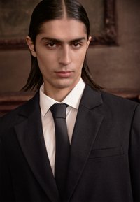 Black suit jacket with a notched lapel, white dress shirt, and black tie; smooth texture, tailored fit, clean lines, and subtle details.