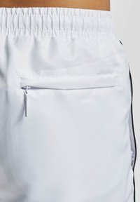 Weiße Sportshorts aus strukturiertem Material, mit elastischem Bund und einer Reißverschlusstasche auf der Rückseite für sichere Aufbewahrung.