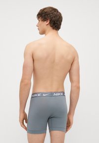 Pelēkie Nike bokseršorti ar zīmola elastīgu jostu. Audums izskatās gluds un pieguļošs, ar īsu kāju garumu un bez redzamām kabatām.