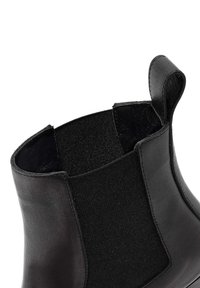 Botín Chelsea de cuero negro con paneles laterales elásticos, textura suave, punta redondeada y tirador en el talón para facilitar su uso.