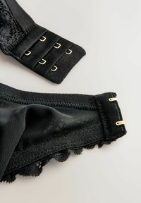 Sort lingerie har et glat stof med blonder detaljer. De justerbare stropper har hardware i guldtonet og krog-lukninger. Tekstureret underlag.
