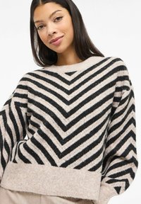 Pull à rayures noir et crème avec un motif chevron, une texture douce, des manches larges et un ourlet côtelé, fabriqué dans un tissu chaud.