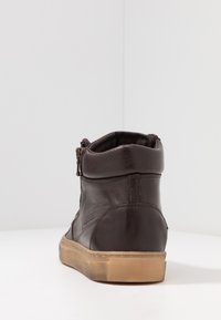 Bottines en cuir marron avec une texture lisse, une forme arrondie, une fermeture éclair sur le côté et une semelle en caoutchouc brun clair. Design simple avec des accents minimaux.