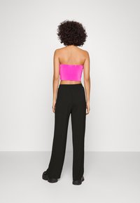 Top rosa aderente senza spalline con texture plissè, abbinato a pantaloni neri larghi. La modella indossa sneakers nere chunky. Sfondo minimalista.