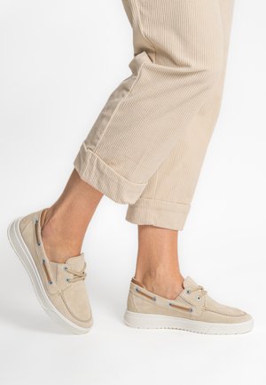 Beige suede slip-on shoes with blue eyelets and cream rubber soles, featuring a rounded toe and a textured finish.