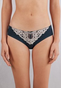 Ciemnozielona bielizna z koronkowymi wykończeniami, ozdobiona delikatnym beżowym haftem kwiatowym z przodu, o gładkiej strukturze materiału i klasycznym kroju majtek.