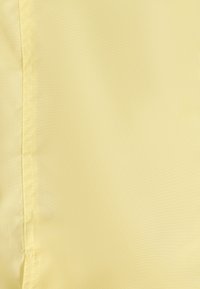 Lichtgele stof met een glad, licht gestructureerd oppervlak; heeft duidelijke naden langs de rand, wat zorgt voor een nette, afgewerkte uitstraling.