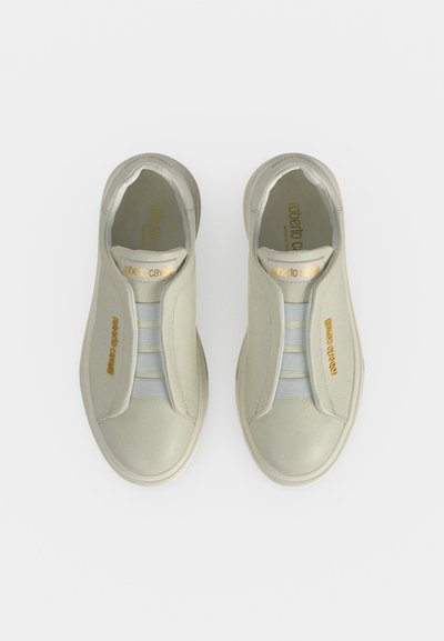 Paire de baskets sans lacets blanc cassé avec bandes élastiques et marquage doré "Roberto Cavalli" sur la languette et les côtés, vues de dessus.