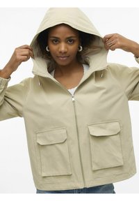 Beige Zip-Jacke mit Kapuze, ausgestattet mit zwei Fronttaschen, elastischen Bündchen und einer glatten Materialstruktur.