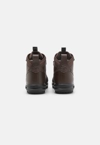 Καφέ ψηλές αθλητικές γόβες με υφή από δέρμα, ενισχυμένη φτέρνα και καουτσούκ σόλα. Διαθέτουν λογότυπο Nike στη φτέρνα και στην ταινία έλξης.