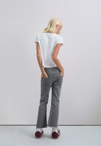 Camiseta blanca corta y vaqueros grises acampanados con un patrón floral rosa, combinados con zapatos blancos y burdeos. Vista desde la parte de atrás.