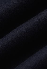 Ciemnoniebieska wełniana tkanina o miękkiej, grubej teksturze. Materiał charakteryzuje się gładkim wykończeniem oraz subtelnymi różnicami w głębokości koloru wzdłuż fałd.