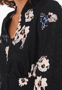 Black floral-patterned fabric featuring textured detailing, buttons, and a deep V-neckline. Accents include light pink and blue flowers.