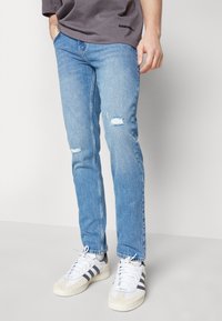 Ljusblå denimjeans med slitna hål, rak passform och kontrasterande sömmar. Matchas med vita och grå sneakers.
