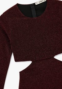 Vestido burdeos hecho de tela texturizada y brillante. Presenta un escote redondo, mangas largas y un detalle recortado en la cintura. Cierre de cremallera en la parte trasera.