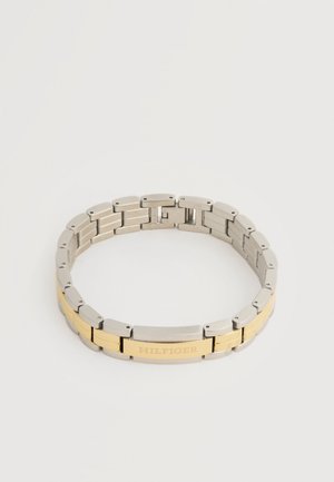Tweekleurige metalen armband met zilveren en gouden schakels, voorzien van een centrale gouden plaat met daarop "HILFIGER" gegraveerd.