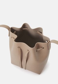 Sac seau tan avec un bord supérieur ondulé, doté de deux sangles latérales et d'une surface texturée. Conçu pour un intérieur ouvert.