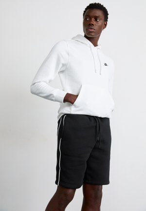 Biała bluza z kapturem z przednią kieszenią i czarnym logo, w połączeniu z czarnymi szortami z białymi paskami po bokach. Gładka tekstura, casualowy design.