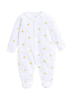 Lachende baby met rood haar die ligt op een grijze deken, gekleed in witte voetjespyjama met gele eendjesprint.