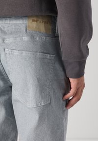 Lys grå denimjeans med en glatt tekstur, med en baklomme og en lys lærdetalj merket "ONLY & SONS." Subtile sømdetaljer.