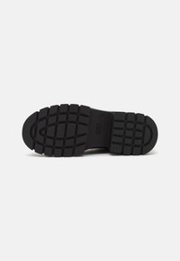 Semelle de chaussure en caoutchouc noir avec un motif de semelle profond et des rainures ; présente un orteil arrondi et un design plat pour la stabilité et l'adhérence.
