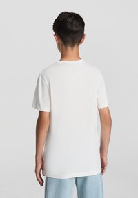 Biała bawełniana koszulka z krótkim rękawem, okrągłym dekoltem, luźnym krojem i prostym dołem. Gładka faktura z minimalnymi detalami szwów.