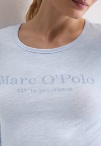 Lichtblauw, kort mouw t-shirt van zacht materiaal, met de tekst "Marc O'Polo" en "OPGERICHT IN STOCKHOLM" in een iets donkerdere tint.