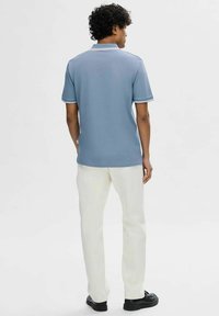 Polo shirt blu con colletto e accenti sulle maniche bianchi a contrasto, abbinato a pantaloni bianchi e scarpe nere; tessuto morbido, vestibilità casual.