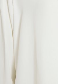Primo piano di un morbido tessuto bianco con sottili pieghe verticali e texture, che mette in risalto il drappeggio fluido e le ombre leggere.