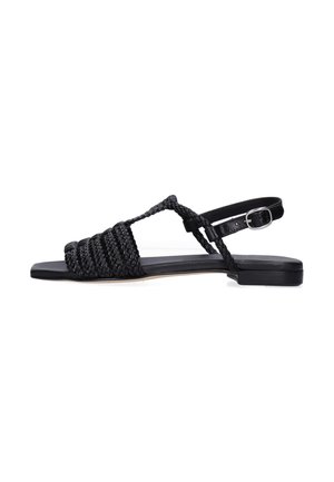 Sandalia plana negra con tiras trenzadas, cierre ajustable con hebilla y suela delgada.