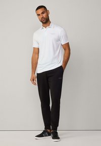 Weißes Poloshirt mit kurzen Ärmeln und hellblauen Akzenten, kombiniert mit schwarzen, taillierten Jogginghosen und schwarzen Sneakers, mit dezenten Markenlogos.