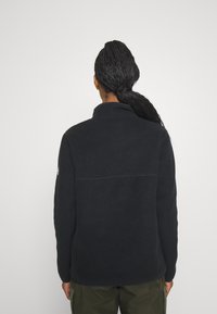 Czarna polarowa kurtka z wysokim kołnierzem, z przeszyciem na plecach i długimi rękawami. Materiał o fakturze, minimalistyczny design.