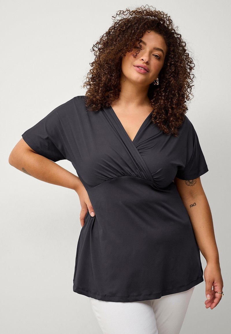 Blouse noire à manches courtes avec un décolleté en V et des détails froncés au niveau de la poitrine. Tissu lisse et léger ; coupe décontractée.