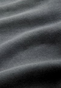 Tmavě šedá pletená látka s detailním pohledem na texturu ukazující jemné, rovnoměrné stehy a měkké záhyby.